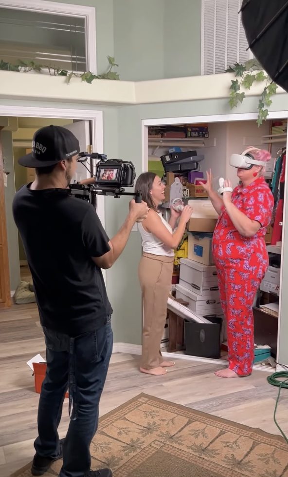 A camera operator filming Unison and a woman in front of a crowded closet