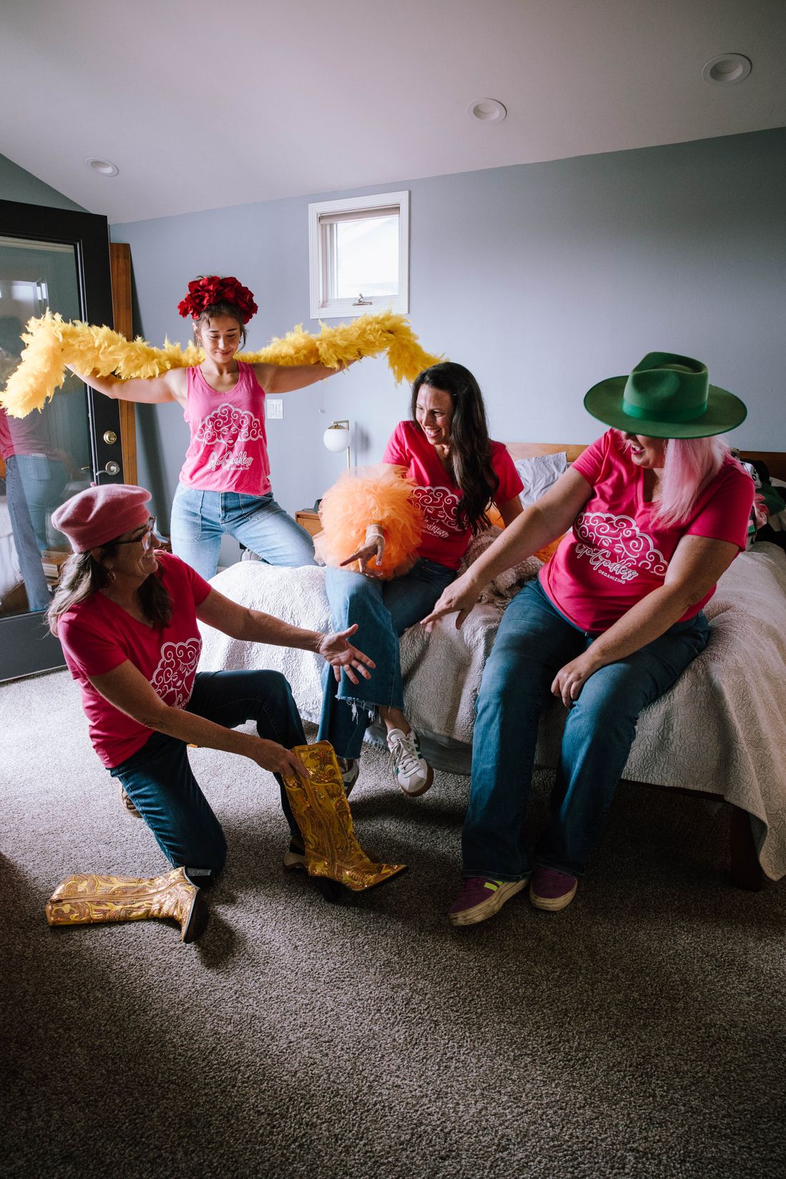 The Goddess Team laughing and playing with a feather boa in a bedroom