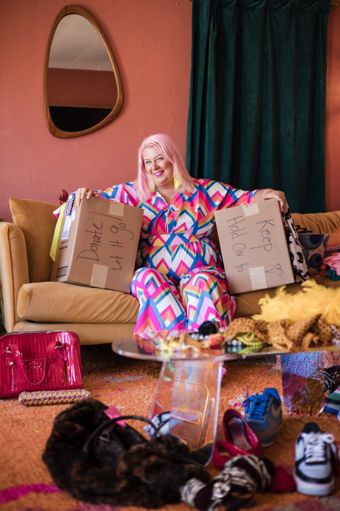 Unison from Go Goddess sits on a couch sorting items into two boxes labeled ‘Keep’ and ‘Throw Away,’ showing her signature decluttering method in action.