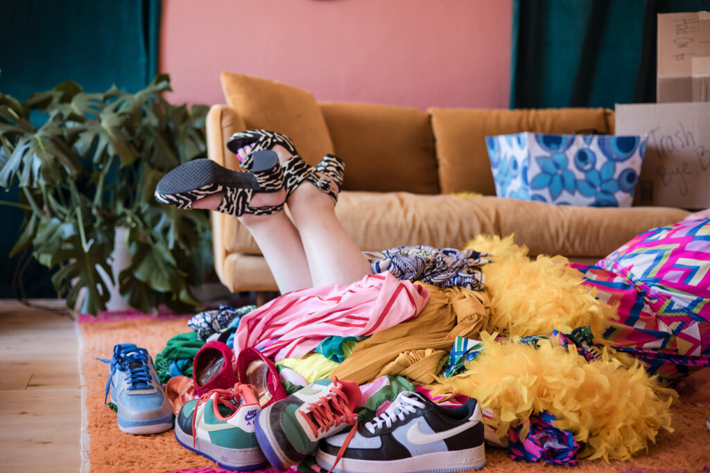 Go Goddess founder Unison playfully kicks up her legs in funky heels surrounded by laundry, reminding women to have fun while getting organized.