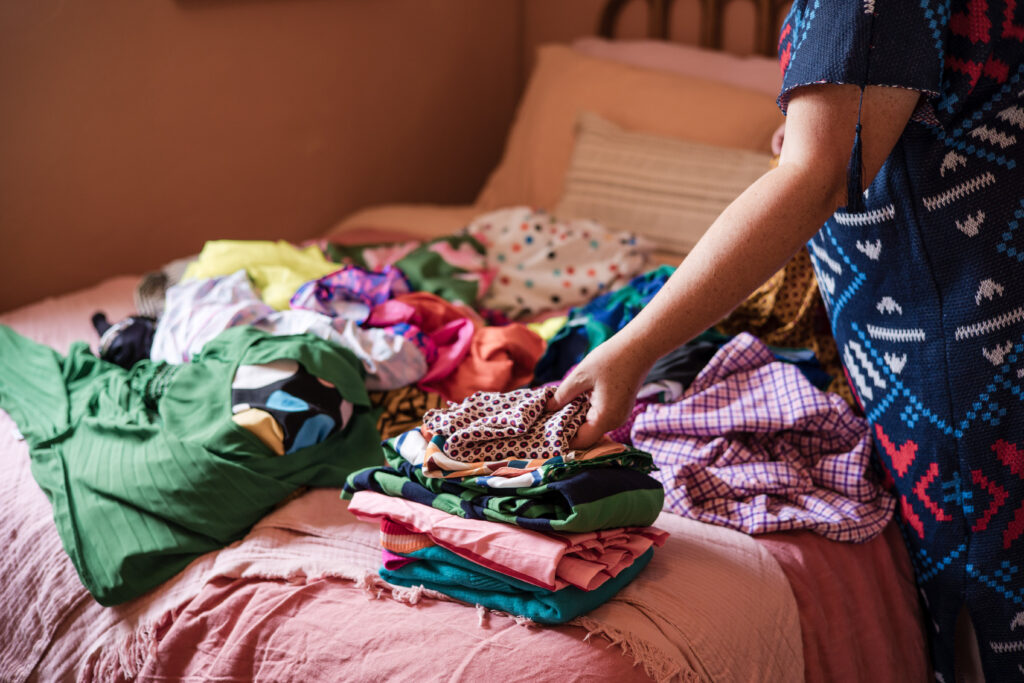Professional organizer Unison from Go Goddess folds piles of laundry on a neatly made bed, showing how organizing can feel calm and empowering.