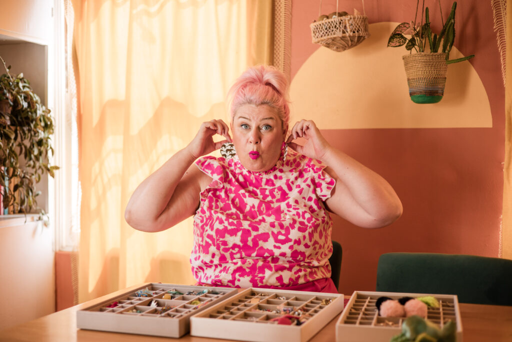 Unison, founder of Go Goddess Organizing, sits at her desk smiling while arranging earrings — inspiring women to declutter with style and joy.
