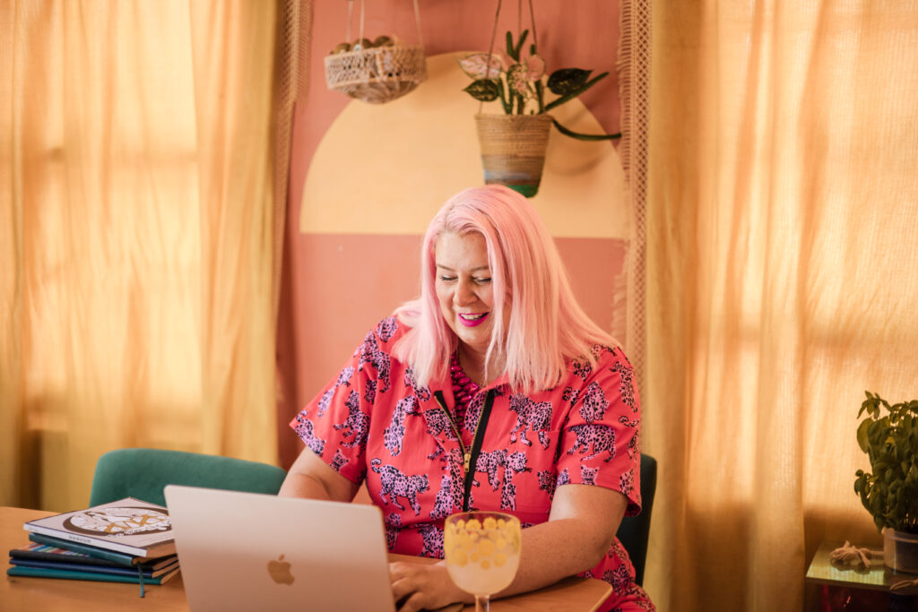 Unison, founder of Unison Creative, working on a laptop in a cozy, colorful home office with plants and warm natural light, personal brand and creative workspace lifestyle.