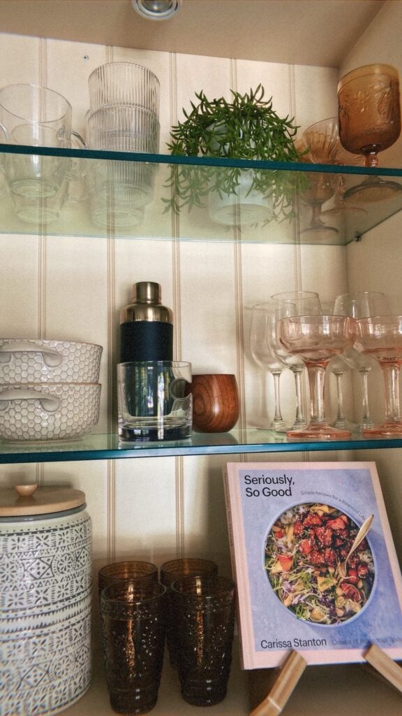Organized kitchen glassware and pantry shelving by Go Goddess Organizing featuring styled cups, cocktail glasses, cookbooks, and decorative storage in a functional, modern cabinet.